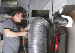 HVAC technician using a large vacuum hose and inspection tools for thorough air duct cleaning service.
