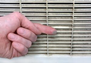 Finger swiping visible dust from a dirty air vent grille, indicating the need for air duct cleaning services.