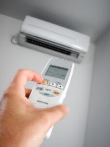 Hand holding remote control pointed at a wall-mounted ductless mini split AC unit, showing mini split installation in use.