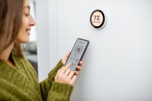 Woman adjusting a smart thermostat using a mobile app, representing modern thermostat repair and control.