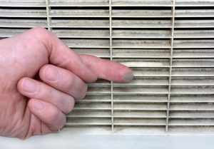 Close-up of a dusty air vent grille with a finger showing accumulated dirt, indicating need for air duct cleaning services.