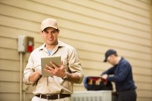 Technicians performing heat pump maintenance with tools and a digital tablet outside a residential building