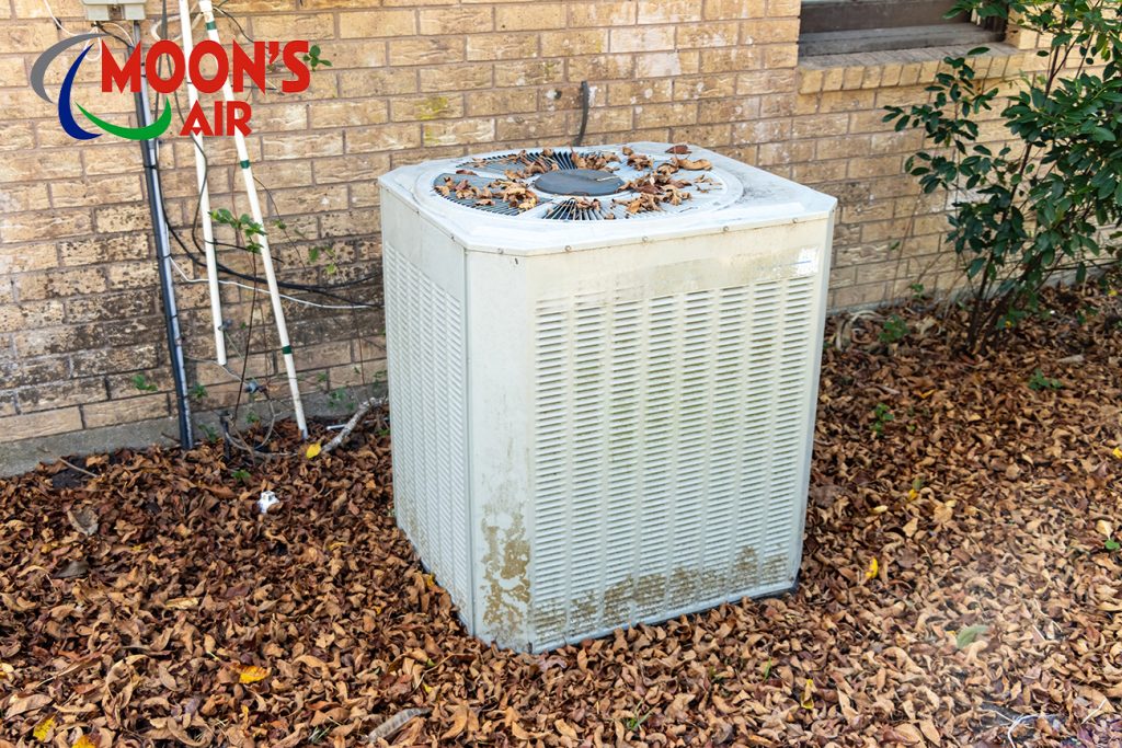 An HVAC unit covered in fallen leaves